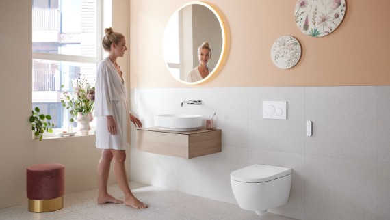 Woman in a bathroom that features a wall-mounted toilet